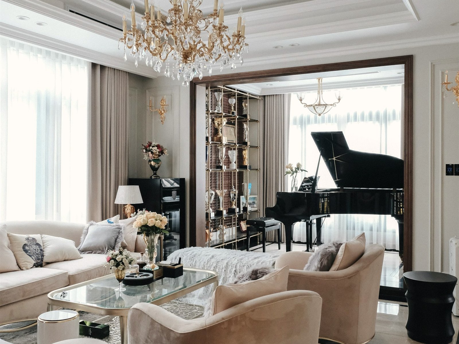 Living room in warm neutrals with a gilded chandelier, brass shelving and champagne velvet seating